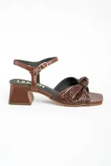 Sandalias de cuero marrón con taco cuadrado medio, tira en el tobillo con hebilla ajustable y diseño trenzado con nudo en la parte delantera.