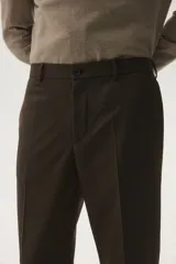Pantalón de vestir color marrón oscuro, corte slim fit, con pliegue marcado en la pierna y puños doblados. Presenta cierre frontal con botón y bolsillos laterales y traseros.