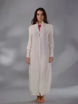 Saco largo de punto color blanco, confeccionado en 100% lana merino natural, con diseño jacquard de ramas, cuello alto, cierre frontal con pequeños botones y aberturas laterales.