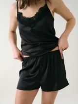 Short para dormir de satén negro, con cintura elástica y botones decorativos frontales.