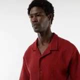 Camisa de manga corta de punto gofrado color rojo, con cuello camisero y cierre frontal de botones.