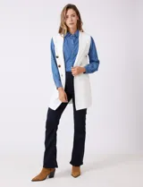 Chaleco largo tejido color blanco de la marca Sioni, con cuello solapa, doble botonadura dorada en el frente y bolsillos aplicados.