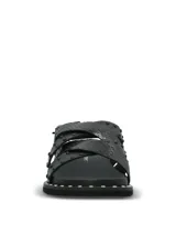 Sandalias negras de cuero con diseño de tiras cruzadas, decoradas con tachas metálicas. Poseen ajuste mediante hebilla lateral y suela de goma con detalle de tachas en el borde.