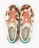 Sneakers de estilo urbano con estampado animal print tipo vaca, confeccionadas en material con textura de pelo. Presentan cordones en tono rosado, detalle de talón en color verde y suela de goma color caramelo.