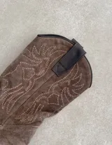 Botas de cuero color marrón y blanco con bordados negros, de estilo cowboy con taco bajo.