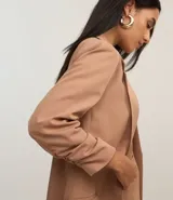 Blazer de sastrería alargado color beige, con cuello con solapa, manga larga con pliegas en el puño y abertura frontal total.