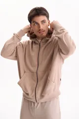 Campera con capucha y cierre frontal, color beige con efecto lavado stone wash, bolsillos tipo canguro y corte oversize.
