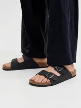 Sandalias estilo Birkenstock color negro con dos tiras ajustables con hebillas metálicas, plantilla anatómica con reborde de corcho y suela de goma.