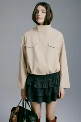Campera beige con cuello chimenea, botones a presión ocultos en la parte delantera, bolsillos superiores con solapa y bolsillos laterales. Cuenta con diseño forrado y ajuste con cordón elástico en el bajo.