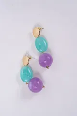 Aros colgantes compuestos por un disco metálico dorado texturizado en la parte superior, seguido de una cuenta ovalada de resina en color turquesa y una cuenta esférica de resina en color violeta.