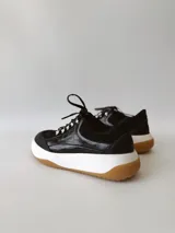 Zapatillas deportivas negras de cuero, con cordones y suela de goma blanca con base marrón.