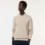 Suéter de punto color beige claro, con cuello polo y tapeta de tres botones. Presenta un tejido texturizado de punto fantasía y puños y bajo acanalados.