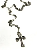 Collar largo estilo rosario plateado, con cadena de eslabones y cuentas metálicas esféricas, decorado con un dije colgante de cruz ornamentada de estilo gótico.