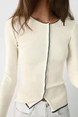 Chaqueta de punto marrón con cuello redondo, manga larga y ribetes en color rojo. Cuenta con cierre frontal de botones.