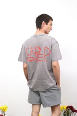 Remera de algodón con efecto lavado ácido en color negro, de corte holgado y manga corta. Presenta un estampado artístico en color rojo en la parte posterior con la palabra Caper.