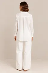 Camisa blanca de manga larga confeccionada en lino y viscosa, con cuello camisero, cierre frontal con botones y delicados bordados florales con apliques de perlas y pedrería en el frente.
