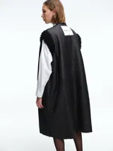 Chaleco largo reversible de diseño versátil. Por un lado, presenta una textura de peluche sintético en color marrón, y por el otro, un acabado liso. Cuenta con cierre frontal de botones y corte recto.