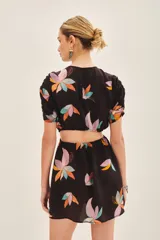 Vestido corto de cuello redondo con estampado floral multicolor sobre fondo negro. Presenta mangas cortas con detalle fruncido en los hombros y aberturas laterales en la cintura.