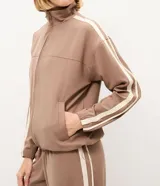 Campera deportiva oversized de microfibra color marrón, con cuello alto, cierre frontal y bolsillos laterales. Presenta bandas laterales contrastantes en las mangas y cordón ajustable en el dobladillo.