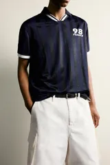 Polo de corte relajado confeccionado en tejido técnico, con diseño de rayas verticales en tonos azul marino y negro. Presenta cuello solapa con abertura frontal y detalles de rib en contraste en cuello y mangas. Incluye estampado frontal con el número 98 y la inscripción France, además de una etiqueta aplicada en el ruedo inferior.