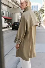 Trench de corte oversize color beige, con cuello alto, cierre frontal de botones y mangas largas con puños vueltos estampados a cuadros. Cuenta con bolsillos delanteros de vivo.