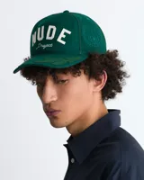 Gorra verde botella de estilo varsity, estructurada, con la inscripción frontal "NUDE Project" bordada en blanco. Presenta detalles de hojas bordadas en tono sobre tono sobre la visera.
