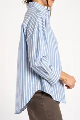 Camisa de algodón con rayas verticales celestes y blancas, de corte oversize, cuello camisero, manga larga y bolsillo aplicado en el pecho.