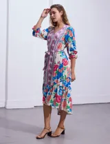 Vestido midi con estampado floral en tonos azules, rojos y blancos. Tiene escote en V, mangas 3/4 con puños fruncidos, cintura elastizada con lazo de ajuste y falda con volantes.