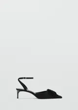 Zapato tipo kitten heel color negro, con punta fina y detalle de pompones en el empeine. Cuenta con una tira ajustable con hebilla en el tobillo.