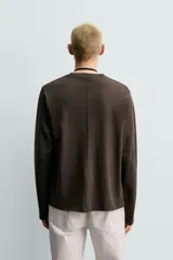 Camiseta de manga larga con corte relajado, confeccionada en tejido de algodón compacto. Presenta cuello redondo y detalle de costura en el centro de la espalda.