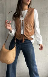 Chaleco de gamuza color camel con bordados decorativos en hilo claro y cierre frontal mediante lazos con borlas. Presenta un diseño de inspiración boho con terminaciones delicadas.