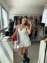 Vestido corto blanco con textura, breteles finos, escote en V, corte ajustado y falda con volados.