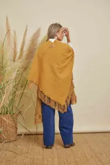 Ruana tejida color mostaza con terminación en flecos de lana y espalda en forma de V.
