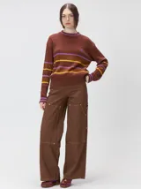 Sweater clásico de punto cable con cuello redondo a la base, mangas largas y fit al cuerpo. De color marrón con franjas horizontales violetas y amarillas, cuenta con el cuello, puños y ruedo acanalados, además de un pequeño logo bordado en el pecho.