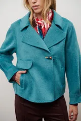 Chaqueta de paño color gris oscuro, con solapas amplias y cierre frontal mediante un alamar único. Presenta bolsillos laterales y mangas largas con puños rectos.