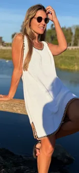Vestido corto blanco tejido en hilo de algodón, con detalles de crochet en contraste negro en el cuello, sisas y ruedo.