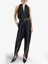 Enterito negro de lana virgen con escote halter profundo y pantalón de inspiración sarouel con cierres metálicos frontales regulables. Incluye cinto fino de cuero negro con hebilla metálica.