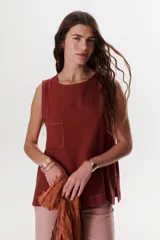 Top sin mangas color celeste claro, con cuello redondo y bolsillo frontal. Presenta costuras a contratono y un pequeño tajo en la parte trasera.