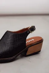 Zueco slingback negro de cuero vacuno con textura grabada geométrica, taco bloque de madera y tira ajustable con hebilla metálica.