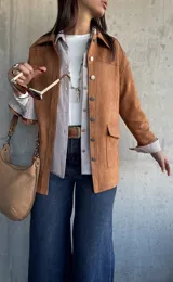 Chaqueta de gamuza color camel, con corte recto, cuello camisero, cierre frontal con botones metálicos y bolsillos frontales con solapa.