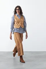 Chaleco de gamuza color marrón, con escote en V y cierre frontal con botones forrados. Tiene un largo a la cintura y silueta definida.