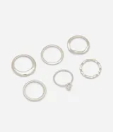 Kit de seis anillos de metal reciclado con diversos diseños, incluyendo aros lisos, texturizados, trenzados, ondulados y un modelo solitario con zirconia en forma de gota.