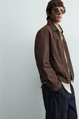 Sobrecamisa de corte regular confeccionada en tejido con estructura canvas color marrón. Presenta un ligero acolchado interior, cuello de solapa y cierre frontal con cremallera metálica. Incluye dos bolsillos de plastrón en el pecho y bolsillos laterales de vivo, con mangas largas terminadas en puños con botón.