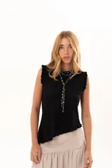 Blusa sin mangas de color negro, con diseño de silueta relajada y terminación asimétrica en pico hacia un lateral. Presenta pequeños volantes en los hombros y está confeccionada en una tela con textura tipo encaje tupido.