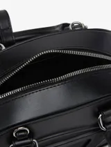 Minibolso estilo bowling color negro, confeccionado en cuero vacuno con forma curva y el logotipo de la D ovalada grabado en la parte delantera. Cuenta con doble asa superior y cierre de cremallera bidireccional.