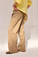 Pantalón de lino lavado color beige, de calce recto y diseño relajado. Presenta cintas de lino desflecadas aplicadas en los laterales con pespunte central, pretina con botón metálico, bolsillos delanteros y traseros.