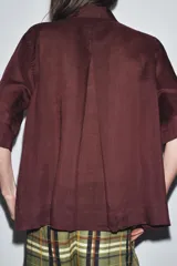 Camisa color borgoña de corte recto, con cuello solapa, manga corta y cierre frontal con botones.