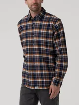 Camisa de manga larga de franela de algodón orgánico con estampado a cuadros en tonos azul marino, mostaza, blanco y marrón. Presenta cuello clásico, cierre frontal con botones de madera y dos bolsillos en el pecho.