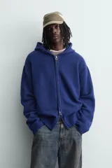 Chaqueta de punto de corte relajado, color azul, con capucha, cierre frontal con cremallera y acabados en rib en puños y bajo.