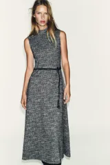 Vestido midi sin mangas, con cuello perkins y cierre de cremallera oculta en la espalda. Presenta un tejido con textura en blanco y negro, y un cinturón fino de efecto piel con anilla metálica. La falda tiene un corte evasé.